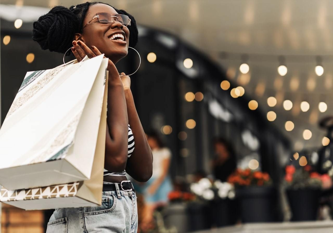 A woman laughs joyfully while holding several colorful shopping bags in her hands.